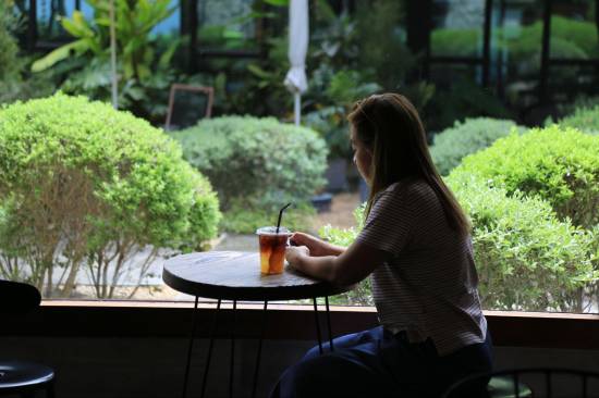 Woman with an iced coffee at a café table by a garden window